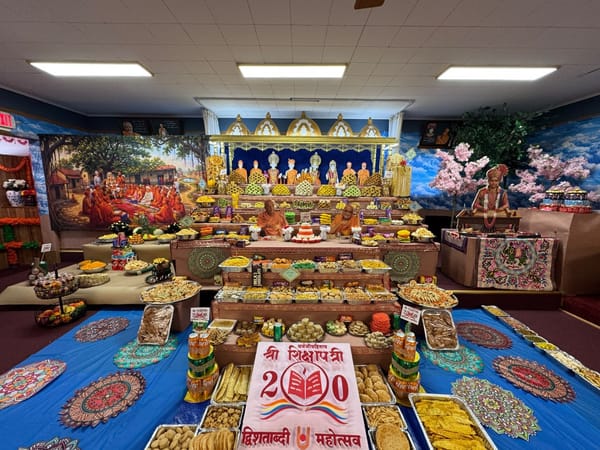 Tiered Annakut offering beneath the murtis, with the Shikshapatri Dvishatabdi Mahotsav sign at the center