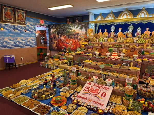 Angled view of the Annakut arrangement with trays of food in the foreground and the murtis behind